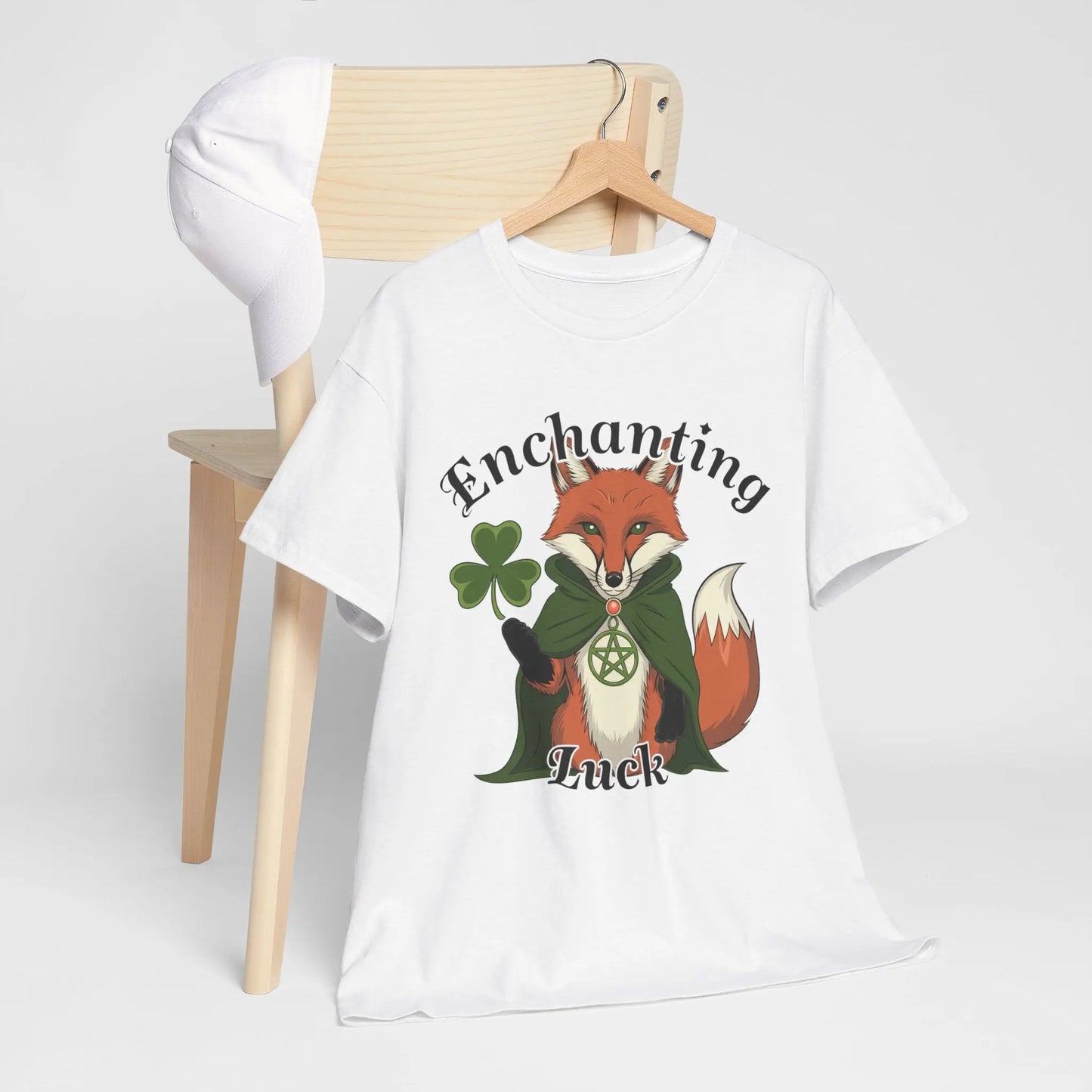 Hanging tee behind a chair mockup, featuring a white tee with a fox design, four-leaf clover, pentagram necklace, and the words 'Enchanting Luck.' witchypets.com